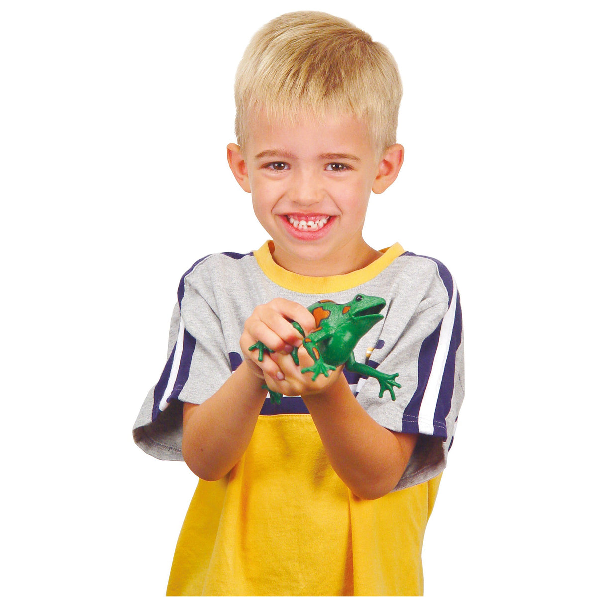 A smiling blond boy in a yellow shirt with gray and blue sleeves holds a Toysmith Frog Squishimals by Toysmith, enjoying sensory play against a plain white background.
