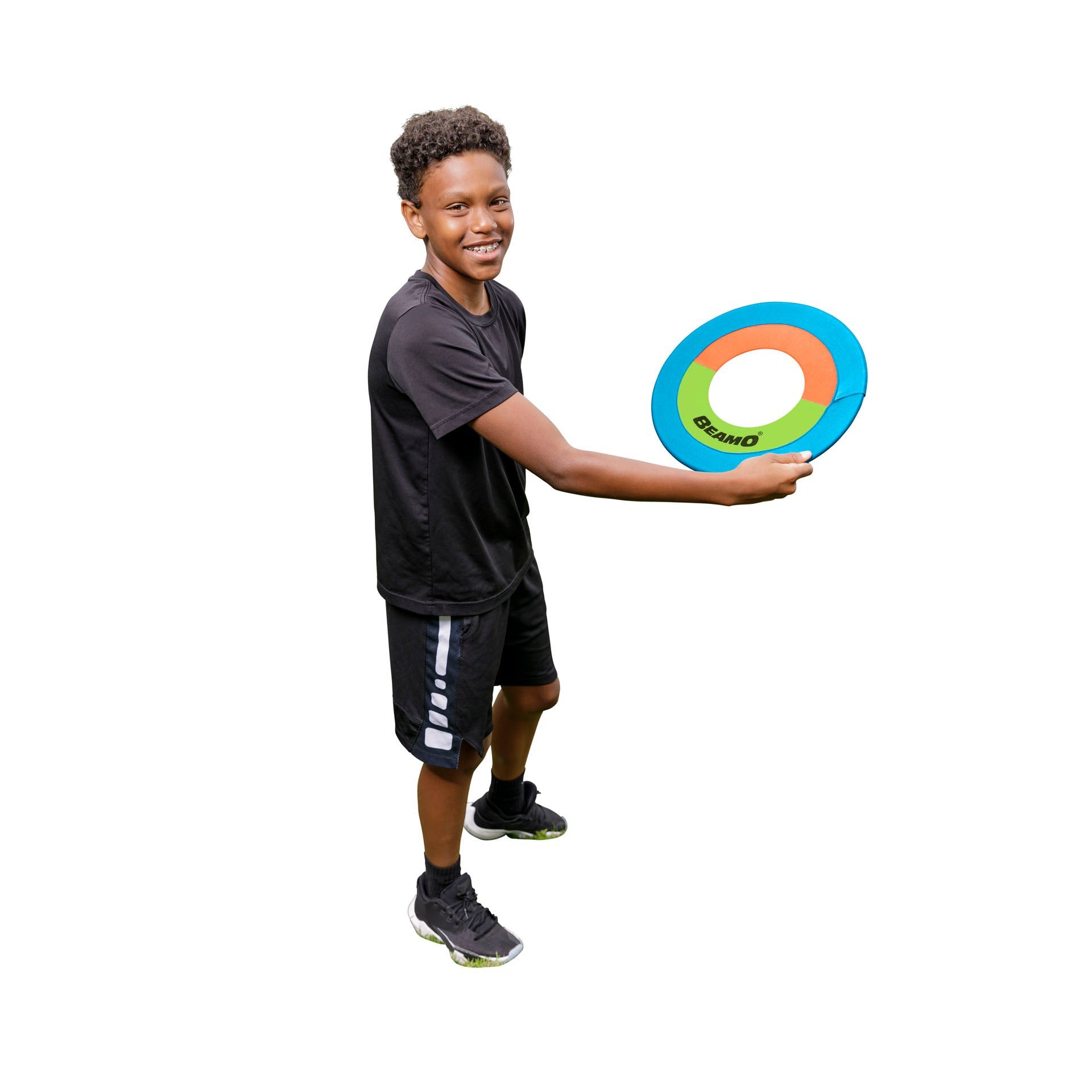 A smiling boy in black outfit and sneakers holds a colorful ring from the GO! Play Triple Play Combo Set by GO! Play, standing against a white background—ideal for keeping kids active and entertained.