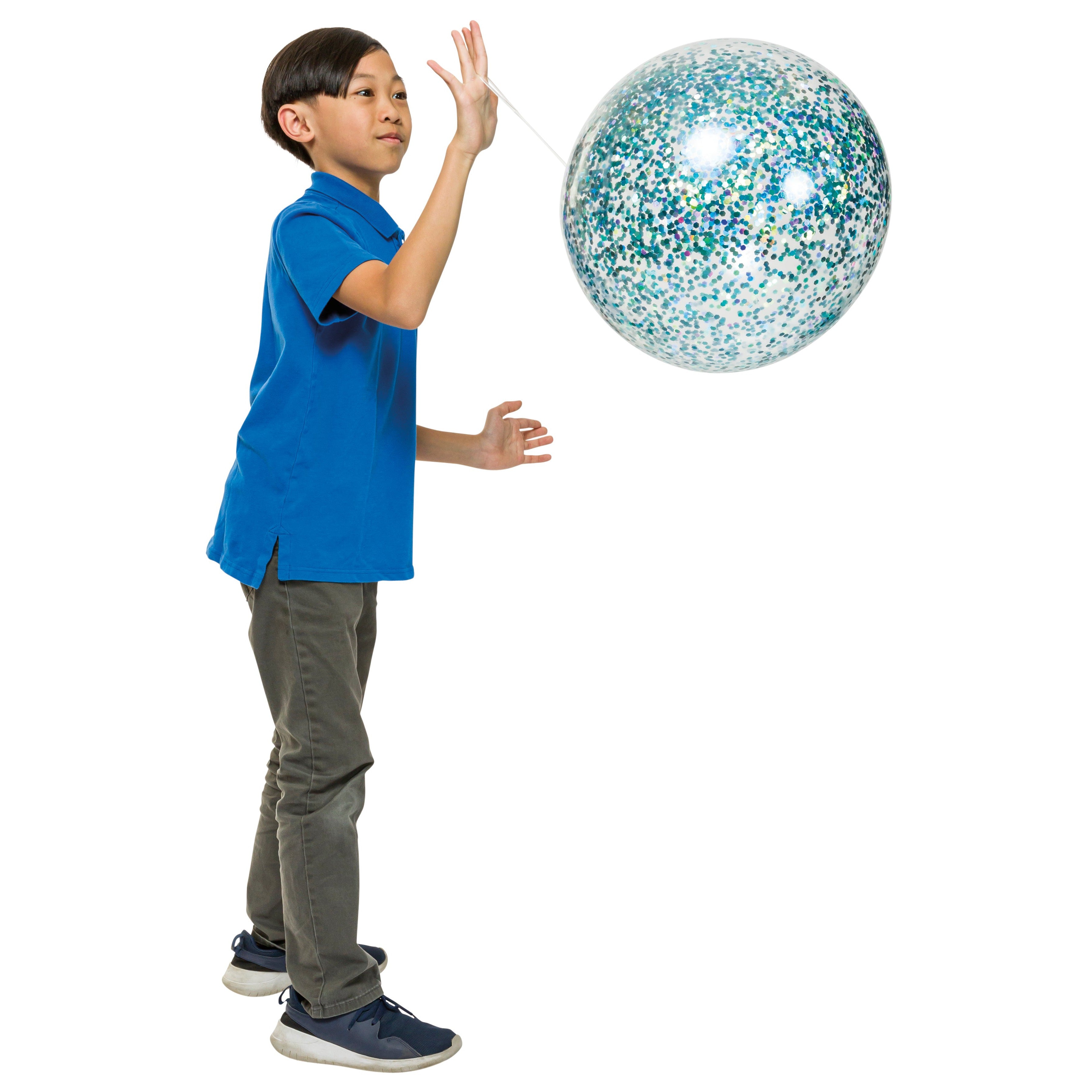 A boy in a blue shirt, gray pants, and blue sneakers stands while tossing a Toysmith Jumbo Punch Balloon with blue and green speckles by Toysmith against a white background.