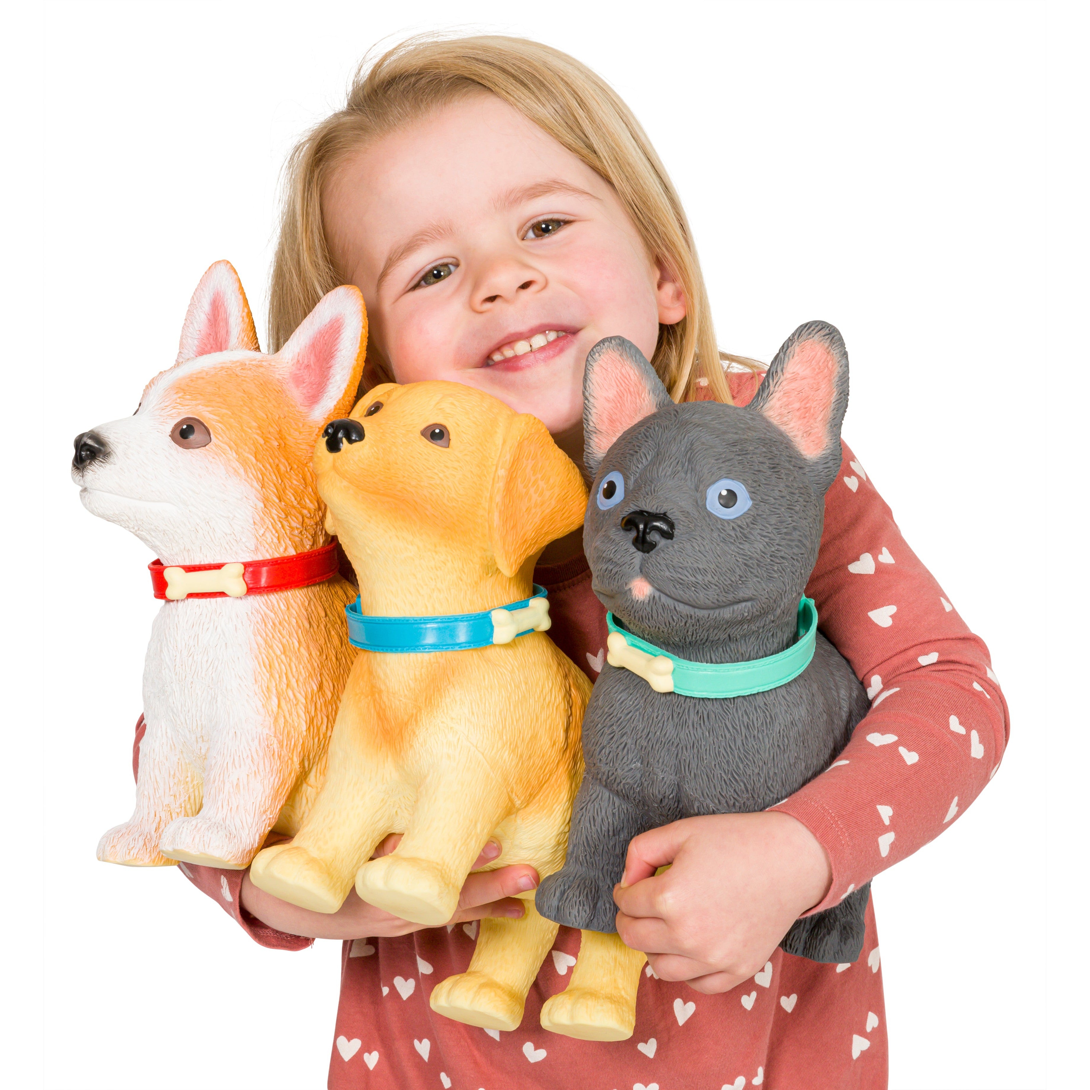 A young child in a pink shirt with white hearts smiles while holding Toysmith Epic Puppies, including the Toysmith French Bulldog figurine and two other colorful collectible pups.