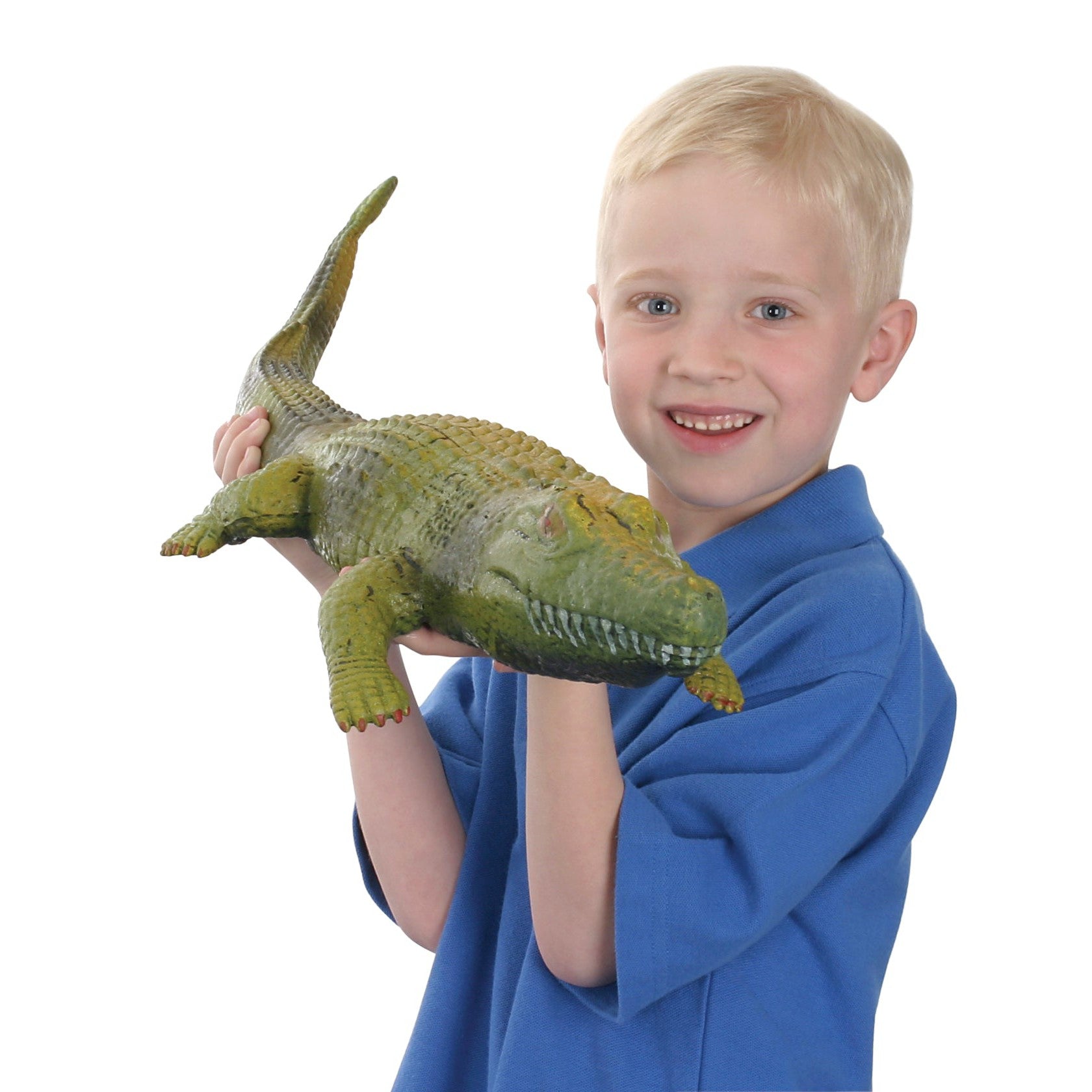 A young boy with short blond hair in a blue shirt smiles while holding the Toysmith Ginormous Grow Crocodile, a realistic water-grow crocodile toy from Toysmith, against a plain white background.