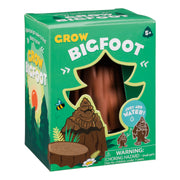 The Toysmith Grow Bigfoot by Toysmith comes in a green box with a tree-shaped window showing the brown toy inside. The packaging features cartoon images of Bigfoot, a bee, a tree stump, and includes a choking hazard warning.