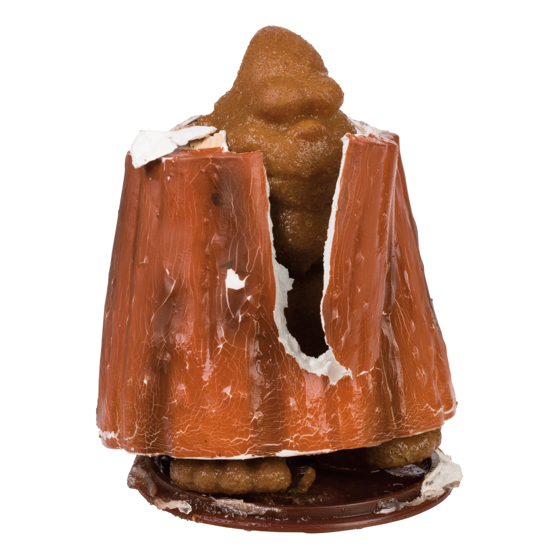 A broken chocolate shell reveals a brown, irregularly shaped Toysmith Grow Bigfoot toy inside, with some white substance at the edges, all set against a plain white background.
