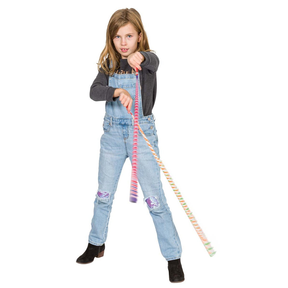 A young girl in overalls and boots stands with arms outstretched, spinning two Neato! Fling Zing Chinese Yo-Yos by Neato! She looks focused as she plays with the colorful, high-energy toys against a plain white background.